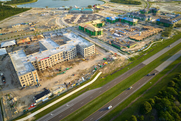 View from above of unfinished frame of apartment condos with wooden roof beams under construction. Development of residential housing near state highway in US suburbs. Real estate market in the USA