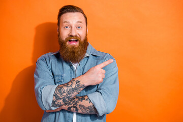 Portrait of cheerful overjoyed cool man indicate finger empty space isolated on orange color background