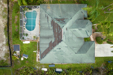 Wind damaged house roof with missing asphalt shingles after hurricane Ian in Florida. Repair of...