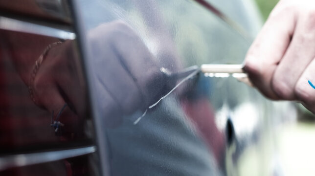 Man scratching car paint with a key, vandalism. Blurred background