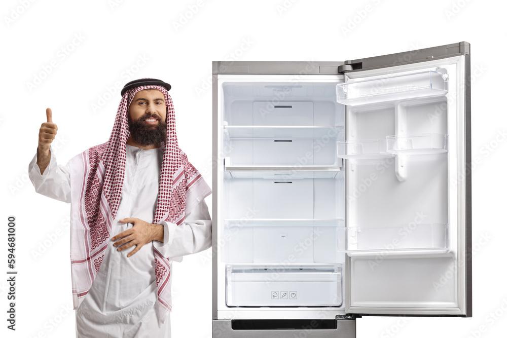 Wall mural sudi arab man leaning on an empty open fridge and showing thumbs up