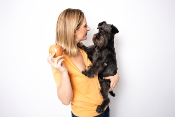 Young woman hugging her dog and playing with an apple standing isolated over white background.