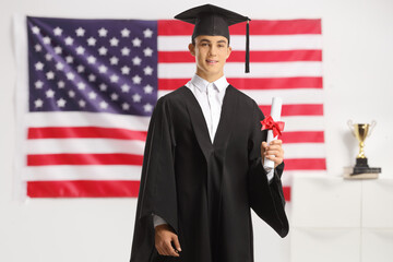 Male teenage student in a graduation gown holding a diploma in front of USA flag