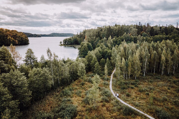 Couple Walking The Hiking Trail Leading To Forest Next To Lake In Early Autumn