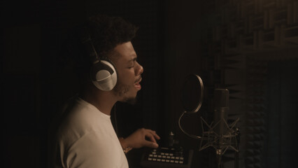 African American vocalist sings lyrical composition into microphone in soundproof room, uses mixing...