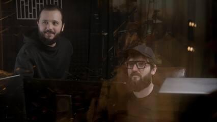 Musical band and experienced audio engineer or producer work on new song in sound recording studio. People look at professional vocalist singing and gesticulate to him. Concept of music production.