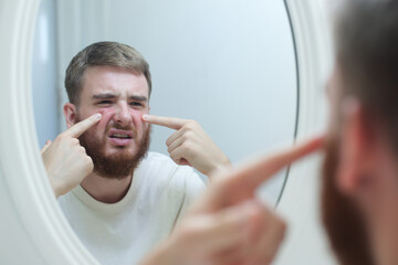 Anxious young man look in the mirror worried about wrinkle or acne on unhealthy skin, upset unhappy millennial female examine squeeze pimple on face in the bedroom, cosmetology, skincare concept 