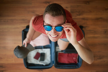 Packing suitcase and planning travel summer adventure. Portrait of happy smiling man with...