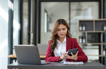 Beautiful asian businesswoman working on laptop and calculating with financial calculator from statistics data graphs, charts. Successful business results in modern office with joy.