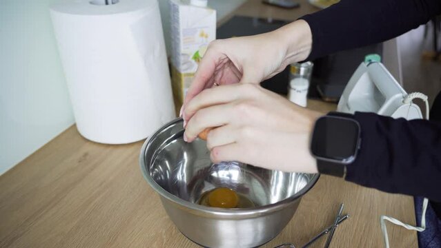 High angle of a woman cracking eggs in the bowl and preparing to beat them to make a cake
