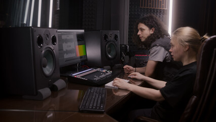 Female audio engineer and singer create song in music recording room. Computer screen showing...