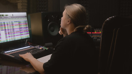 Experienced audio engineer or producer works in sound recording studio. Woman uses mixing console and digital audio workstation software to create new song. Program for recording music on PC monitor.