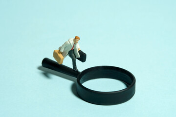 Miniature tiny people toy figure photography. A man wearing with coat running above magnifier glass. Isolated on blue background.