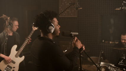 African American vocalist keeps hands on professional microphone stand and sings new composition in...