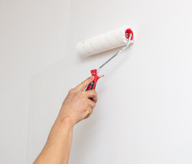 A worker paints the walls in a room with white paint with a roller.