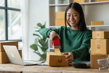 Fototapeta na wymiar starting a small business Asian young woman business owner using masking tape to stick Close the parcel box, prepare for delivery through the shipping company according to the received online order.