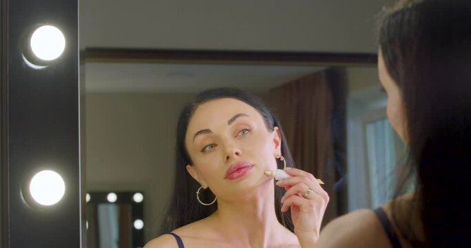 Young Caucasian woman applying makeup foundation in fromt of mirror at home.