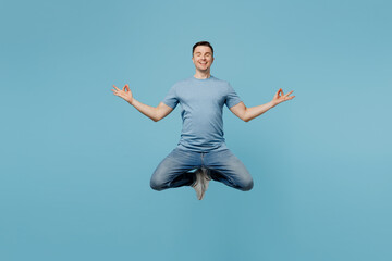 Full body young smiling happy man wear casual t-shirt jump high hold spreading hands in yoga om aum gesture relax meditate try to calm down isolated on plain pastel light blue cyan background studio.