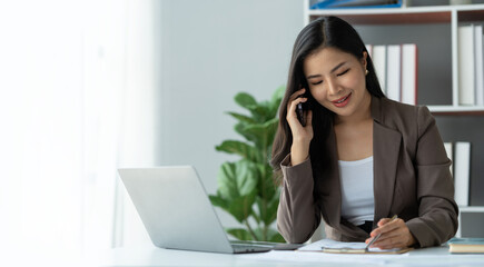copy space, panorama ,banner , Happy young asian woman talking on the mobile phone and smiling while sitting at her working place in office.