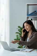 Happy young asian woman talking on the mobile phone and smiling while sitting at her working place in office.