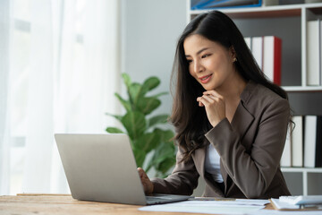 Asian businesswoman, self-employed working on laptop computer typing e-commerce marketing financial report on real estate project in office management concept.