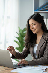 Asian businesswoman, self-employed worker working on laptop computer looking at data and pointing at e-commerce marketing finance report in real estate project in office management concept.