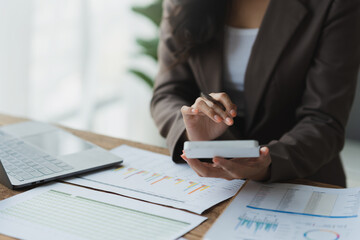 Asian businesswoman recording data using desktop computer keyboard and calculator to analyze marketing strategy and real estate data reduce corporate taxes for clients. Accounting and Tax Concepts