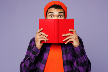 Young surprised smart clever student man of African American ethnicity wear casual shirt orange hat read novel cover mouth with book at library isolated on plain pastel light purple color background.