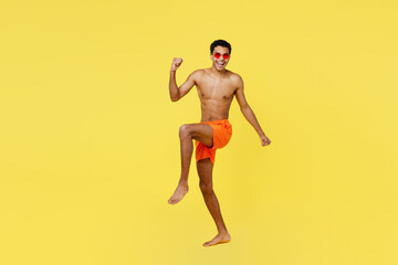 Fototapeta na wymiar Full body overjoyed happy young sexy man wear orange shorts swimsuit relax near hotel pool look camera do winner gesture isolated on plain yellow background. Summer vacation sea rest sun tan concept.