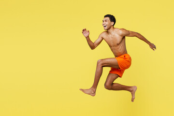 Fototapeta na wymiar Full body young fun sporty man wears orange shorts swimsuit relax near hotel pool jump high look aside on area run fast isolated on plain yellow background. Summer vacation sea rest sun tan concept.