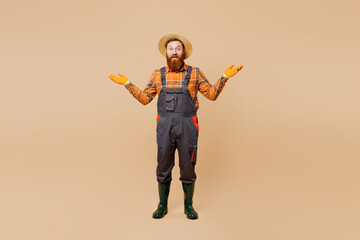 Fototapeta na wymiar Happy shocked surprised young bearded man wears straw hat overalls work in garden look camera spread hands isolated on plain pastel light beige color background studio portrait. Plant caring concept.