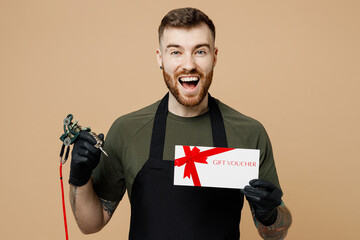 Fun tattooer master artist tattooed man wear green t-shirt apron hold store gift coupon voucher...