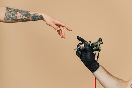 Close up cropped photo of tattooer master artist male hold in hand machine black ink in jar, equipment for making tattoo art on body, touch female finger arm isolated on pastel plain beige background.