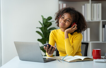 Startup businesswoman, American woman African woman wearing headphones music and holding mobile phone using bluetooth listening music while sitting resting after work happily and relaxing at office.