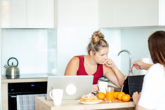 Two Young Pretty Women Sitting With Laptops Facing Each Other, Orange Juice Is Between Them, Fresh Pastries Are Lying. 