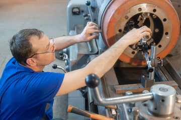 Turner with glasses working at lathe on shop floor. Turner aligns brake disc of truck on lathe..