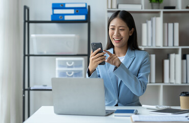 Asian businesswoman using mobile phone Laptop computer in private office to communicate through online applications and happy smile startup business ideas.