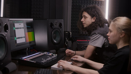 Fototapeta na wymiar Female audio engineer and musician create song in music recording room. Computer screen showing DAW software interface with sound track. Modern equipment in sound recording studio. Music production.