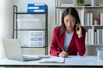 Asian businesswoman using mobile phone discussing financial data from graphs, statistics, income, taxes, company accounts on desk. business idea startup contact.