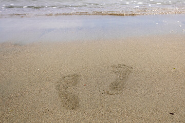 Two footprints on wet sand beside sea wave at the beach