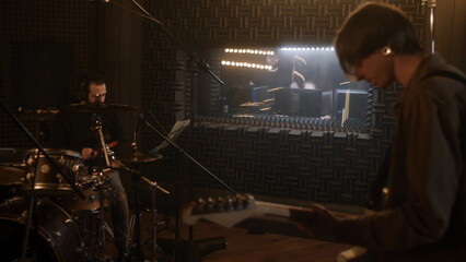 Vocalist sings lyrical composition into microphone in sound recording studio. Musical band record album in soundproof room. Audio engineer looks at musicians work. Music production concept. Back view.
