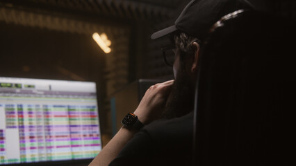 Sound engineer sits at computer and edits song in professional recording studio. Program and tools for creating music on PC monitor. Work in music recording room. Music production concept. Back view.