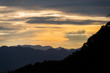 Layers of Silhouetted Mountains at Dusk with Orange Sky and Clouds