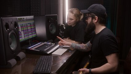 Audio engineer and producer, man and woman, create song in recording room. Computer screen showing...