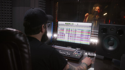 Male singer sings song in soundproof room. Audio engineer, producer uses professional DAW software...
