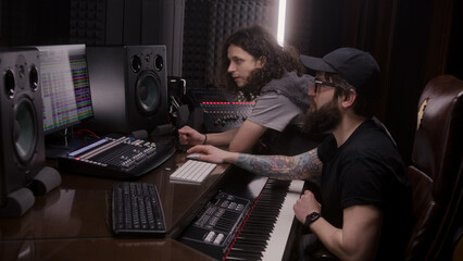 Sound engineer and musician create and listen song in music recording room. Computer screen showing DAW software interface with sound tracks. Work in sound recording studio. Music production concept.