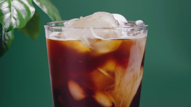 Pouring milk into iced cold brew coffee. Green biophilic background. Close up. Rotation 360 degree
