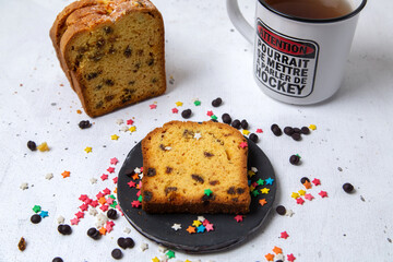 front close view slice of cake inside dark plate with colorful candies and cup of tea on the light...