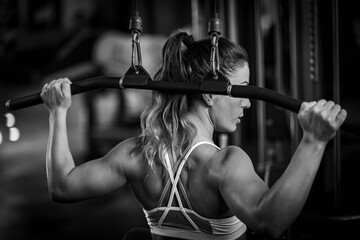 Female athlete exercising on a lat machine in a gym, black and white