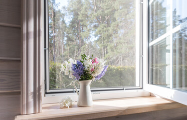 White window with a mosquito net in a rustic wooden house. Spring bouquet of hyacinths on the...